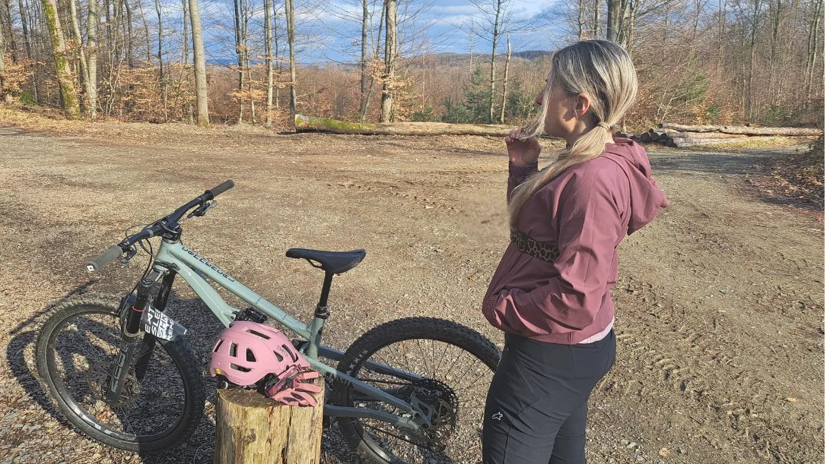 Vanessa steht mit ihrem Mountainbike im Wald und isst einen Energieriegel.